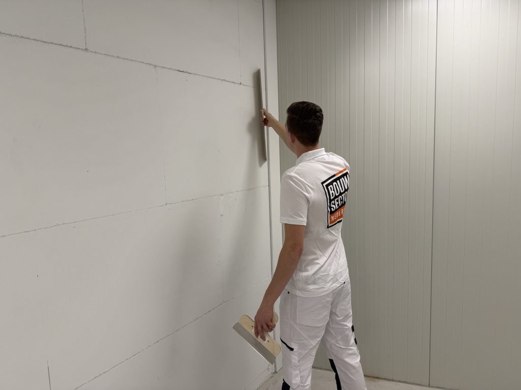 Stukadoor trekt met een lange spaan een naad in een wand vlak en houdt de plakspaan in zijn andere hand