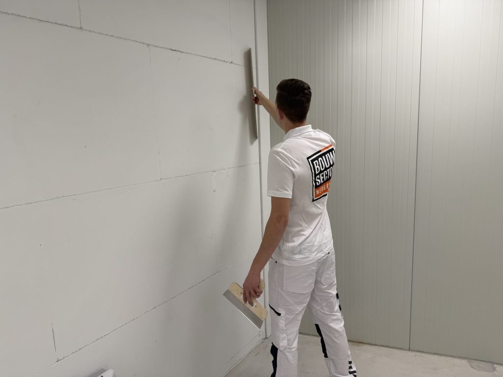 Stukadoor werkt een lange verticale naad in een grijze wand af