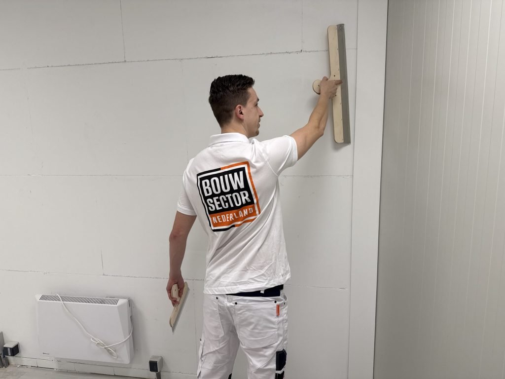 Stukadoor met plakspaan in de hand strijkt met de lange spaan over het bovenste deel van een wand