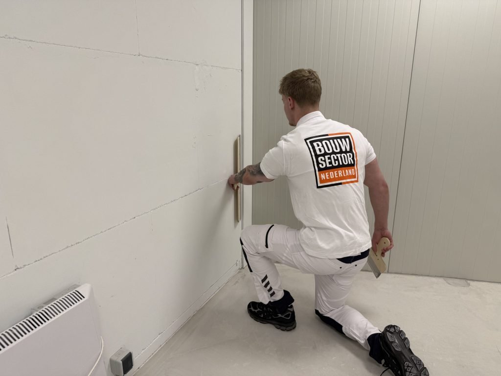 Stukadoor op één knie werkt met de spaan het onderste stuk van een wand bij